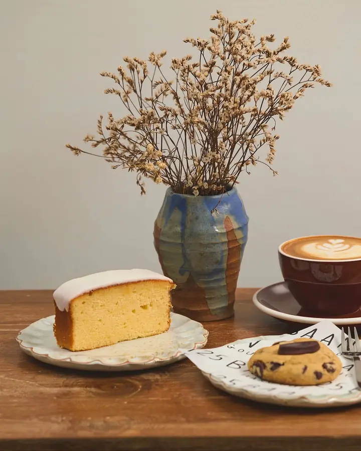 A slice of baan125's signature lemon cake with a latte and a cookie, served on handmade pottery