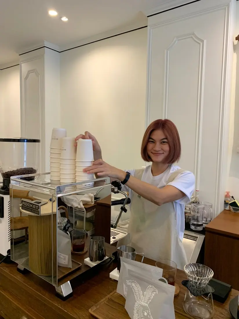 Milk behind the Rocket espresso machine at baan125, stacking cups with a warm smile